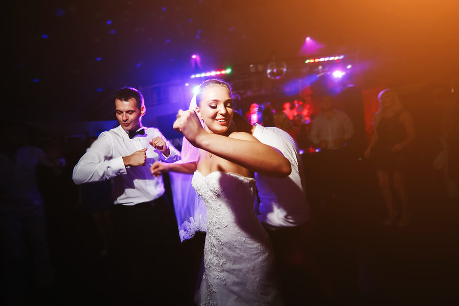 A bride and guests dancing under colored lights at a wedding reception